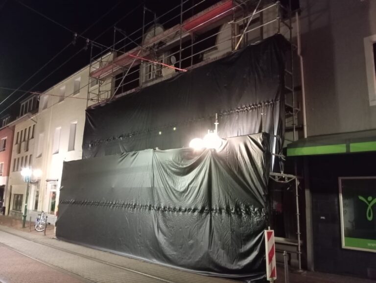 Fassadengerüst in Bonn-Beuel bei Nacht, zur Straßenbahn hin mit EPDM-Kautschukfolie abgehängt