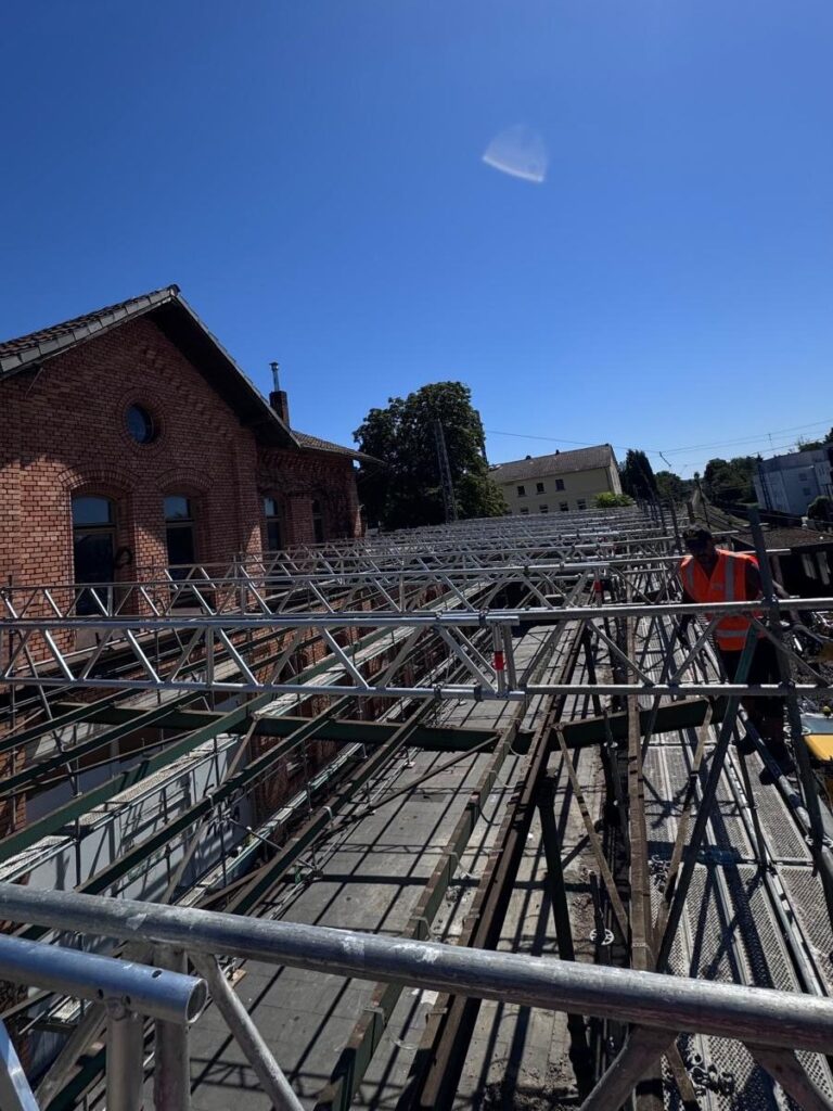 Monteur auf der Dachkonstruktion der Einhausung am Bahnhof Niederdollendorf, Gitterträger vor blauem Himmel
