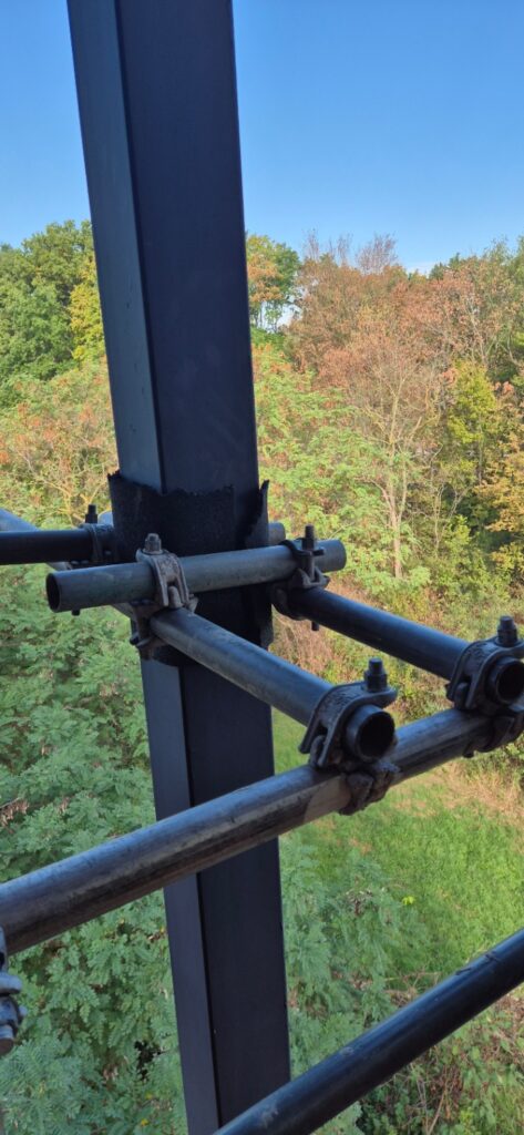 Gerüstrohre mit Kupplungen an einer Stahlstütze des Glasturms, mit Kantenschutz unterlegt
